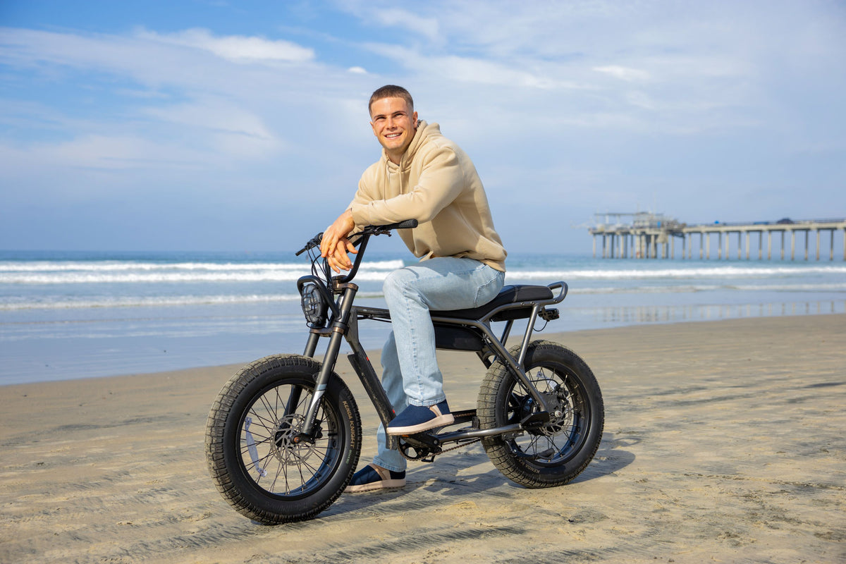 Man riding a electric bike on a beach with a pier in the background #color_navy
