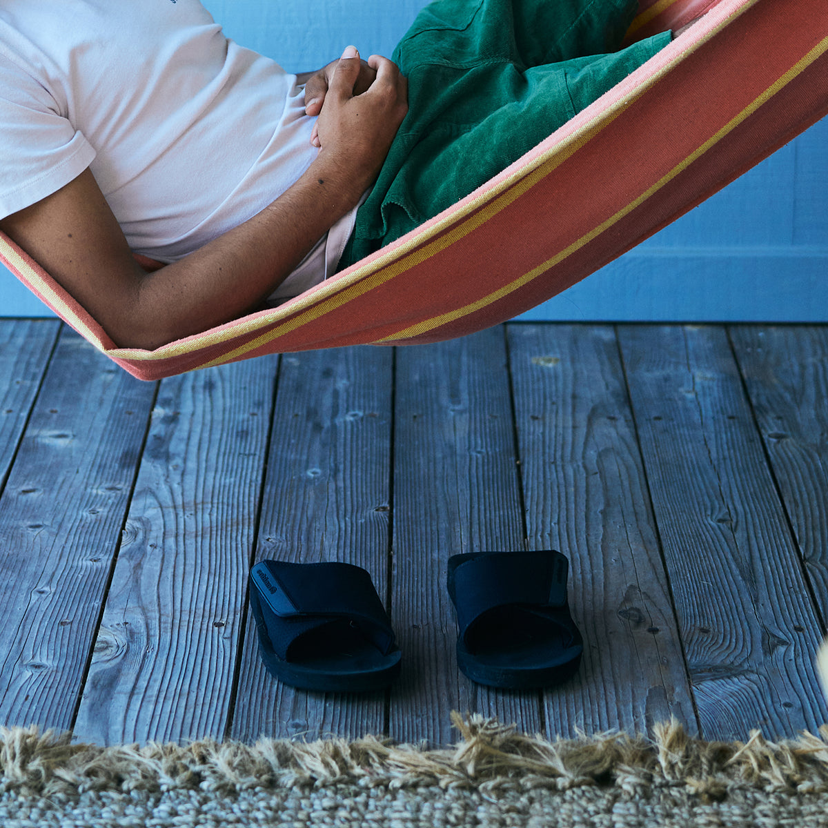 Cobian Model laying in hammock with ARV 2 Slide Black on wood floor below #color_black