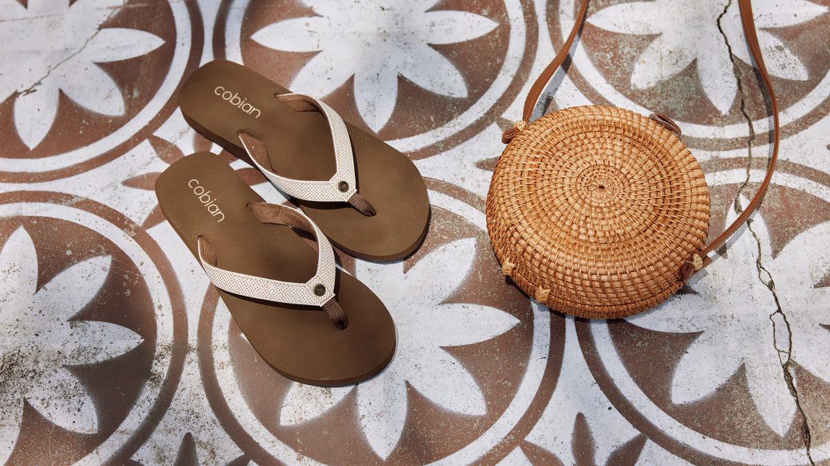Cobian Fiesta Skinny Bounce Tan on flower patterned floor next to a woven bag #color_tan