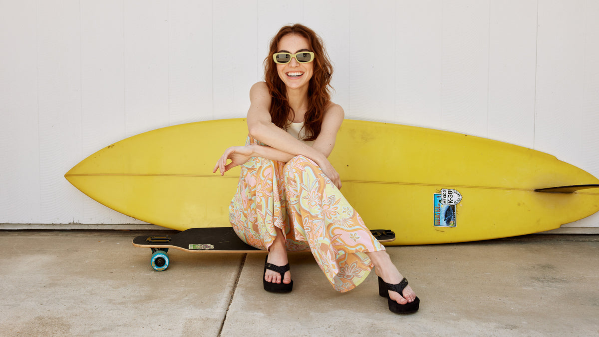 A woman sitting on a skateboard wearing the Cobian Zoe Black Wedge sandal