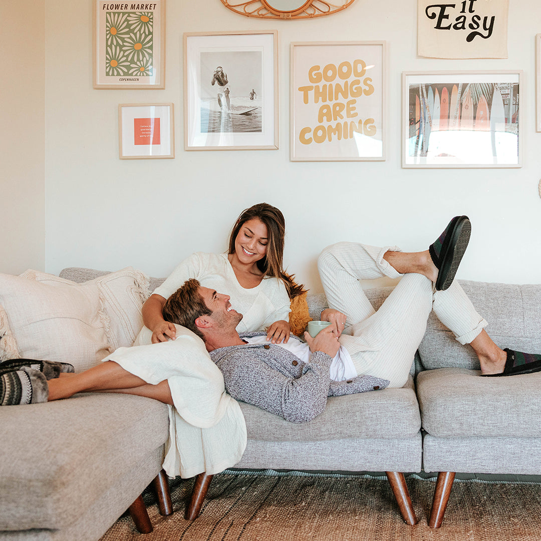 Couple smiling and lounging on a light gray sectional sofa in a bright living room with framed wall art.